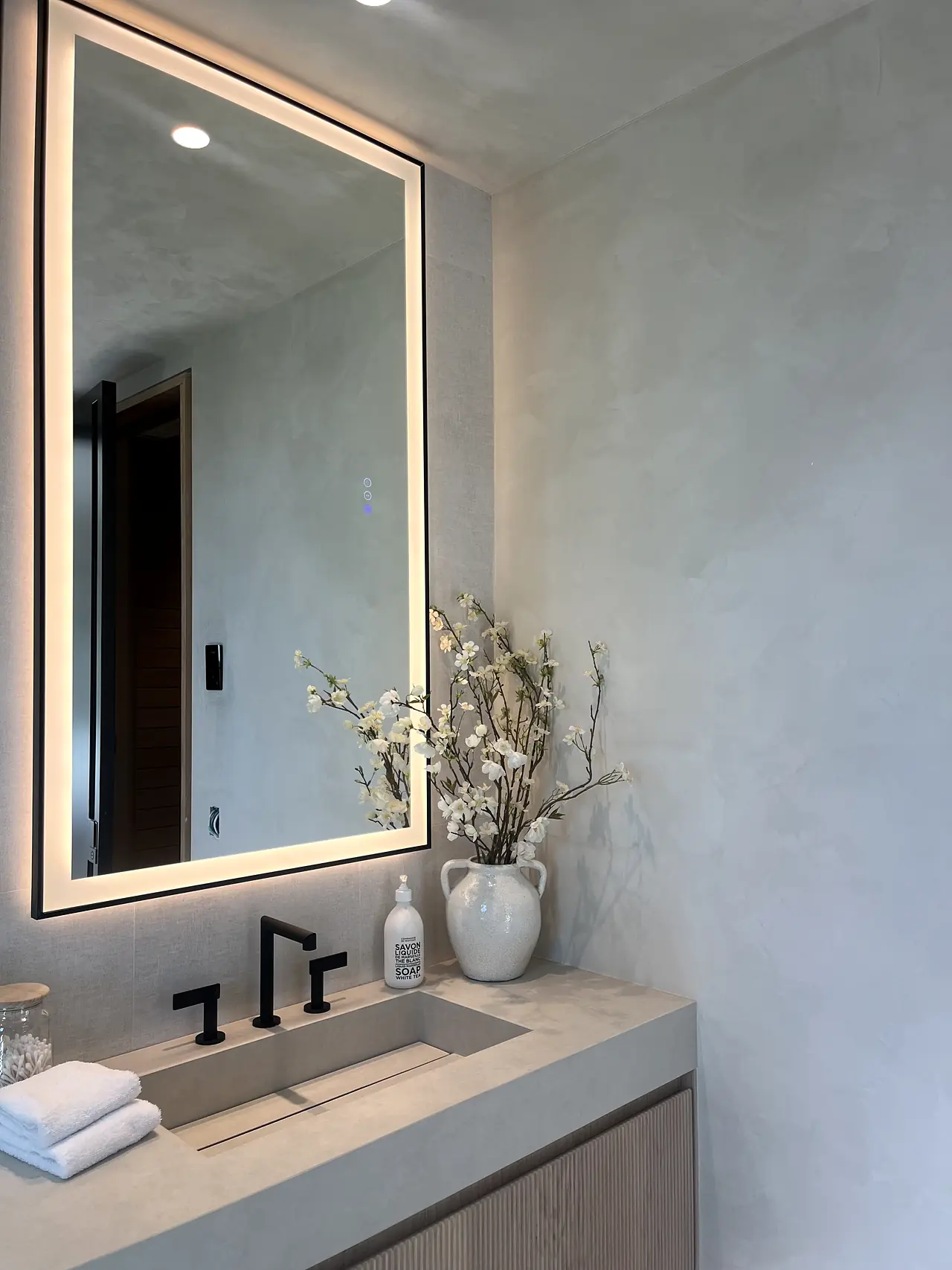 Microcement bathroom vanity wall with a backlit mirror in a Los Angeles home