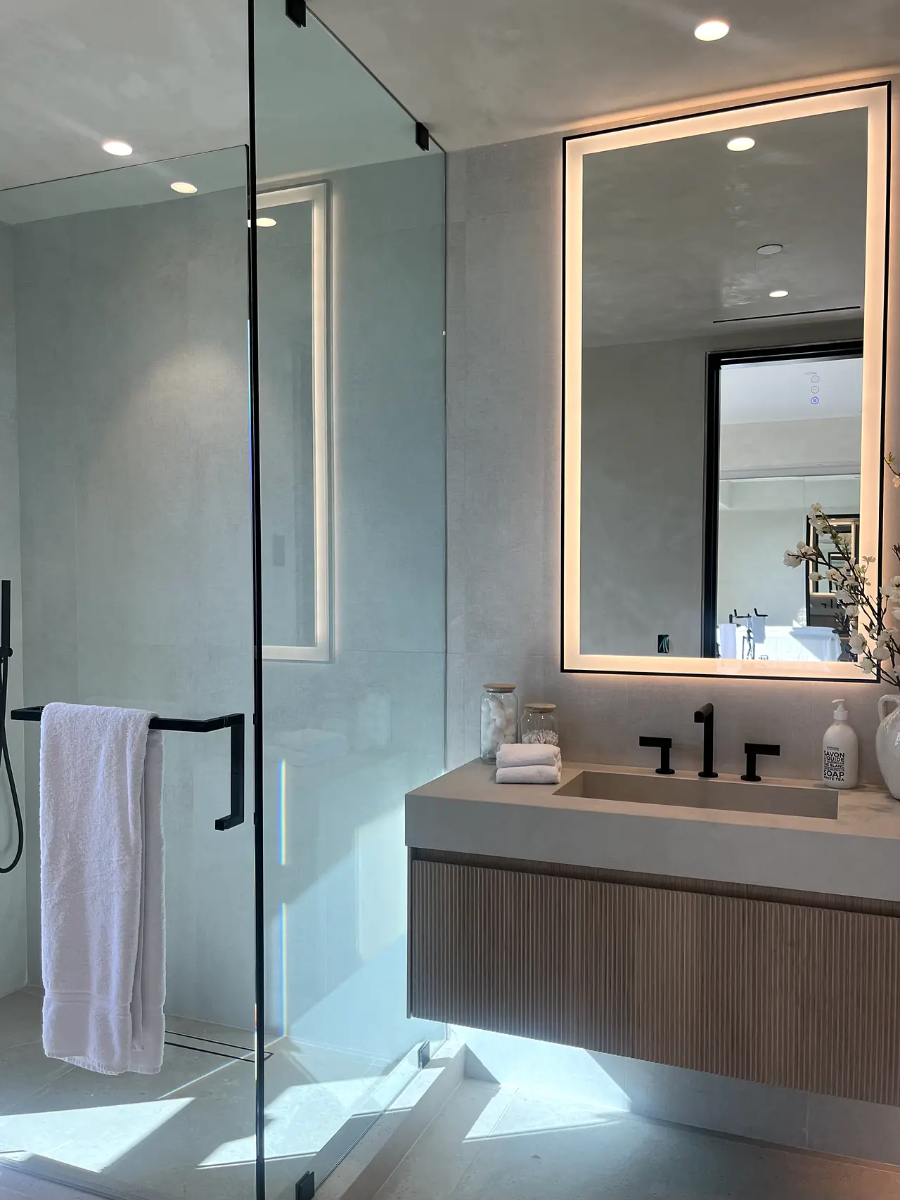 Microcement bathroom walls with a glass shower and backlit mirror in a Los Angeles home