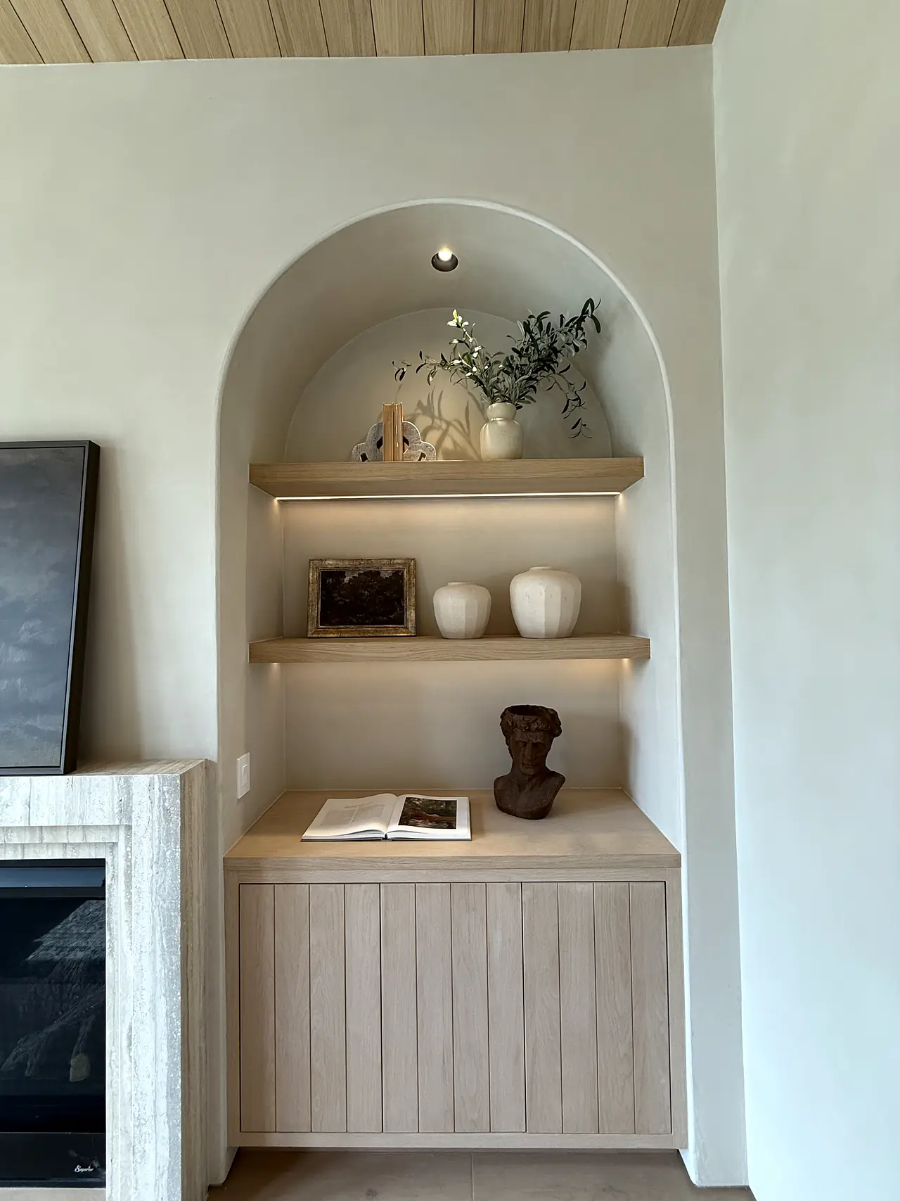 Plaster arched niche with lit oak shelves beside a fireplace