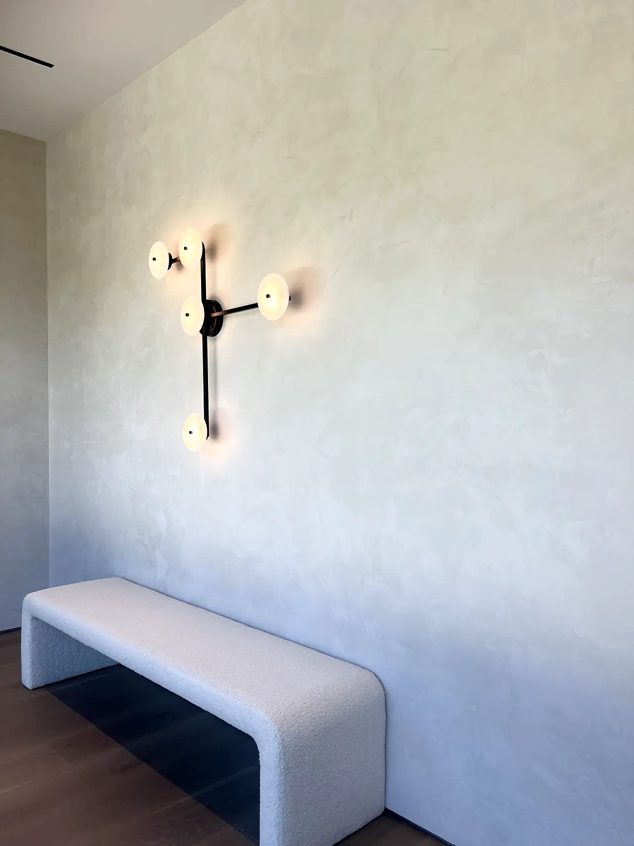 Venetian plaster entry wall with a sculptural sconce and bench in a Los Angeles home